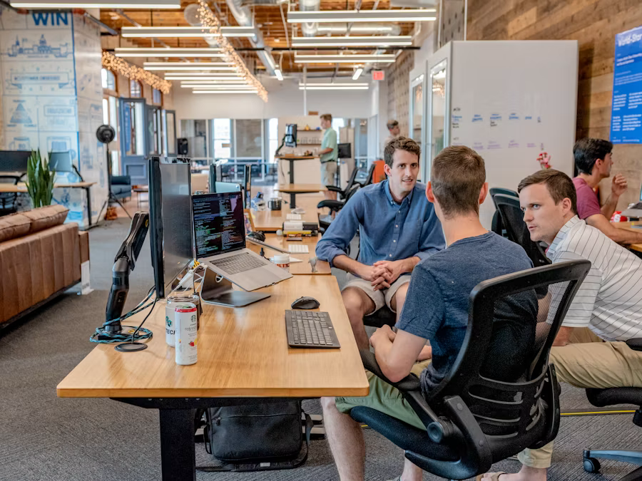 Colleagues discussing Beneficial Shareholder Services at a modern open-office workstation with laptops and monitors.