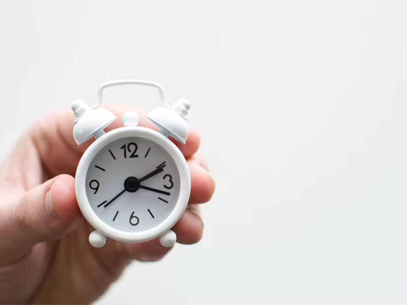 Hand holding a tiny white alarm clock to represent faster turnaround for efficient business solutions.