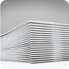 Stack of white saddle-stitched bindings and booklets highlighting the stapled spines on a light gray background.