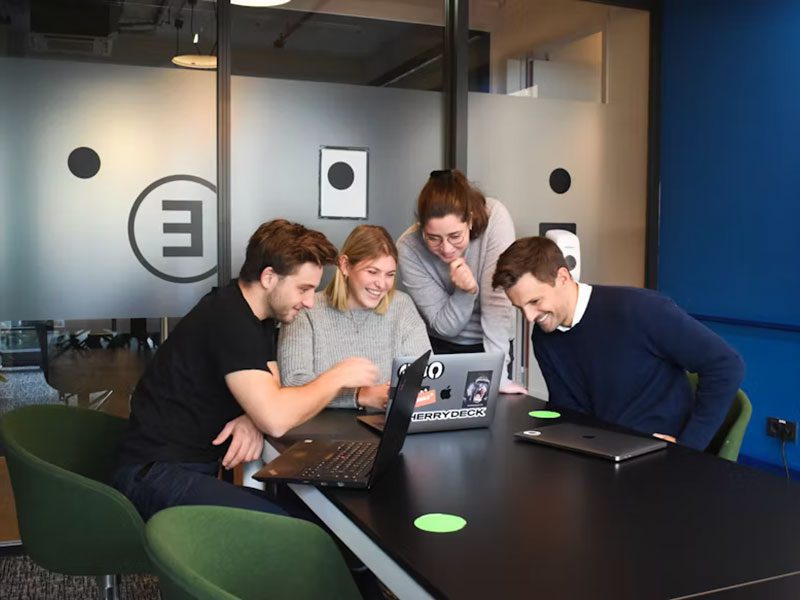 Smiling team collaborating on EDGAR Filing documents at laptops in a modern office