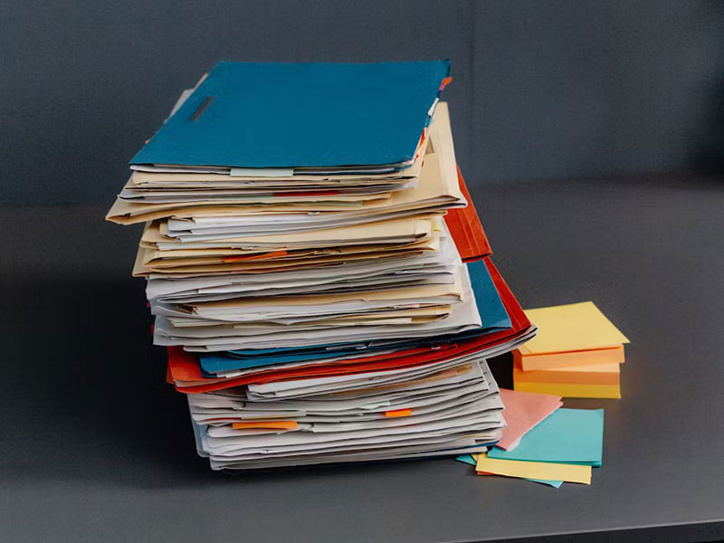 Large stack of colorful office folders and sticky notes representing Unlimited Filing Packages on a dark grey desk.