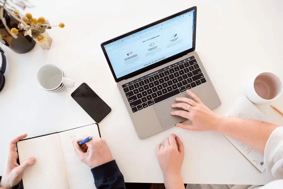 Two people collaborating at a desk with a laptop and a notebook, performing Automated Pre-Filing Checks for a project.