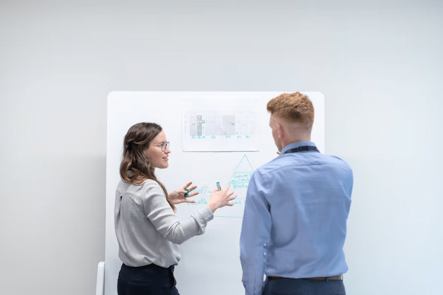 Two colleagues discuss project strategy, charts, and upcoming SEC filing deadlines on a whiteboard.