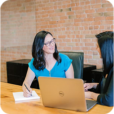 Professional woman in blue taking notes during a free consultation in a modern brick wall office with a laptop on the desk.