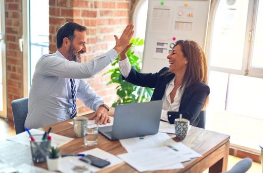 Colleagues high-five over a laptop and papers, highlighting 24/7 Accessibility in their sunlit office workspace. Colleagues high-five over a laptop and papers, highlighting 24/7 Accessibility in their sunlit office workspace.