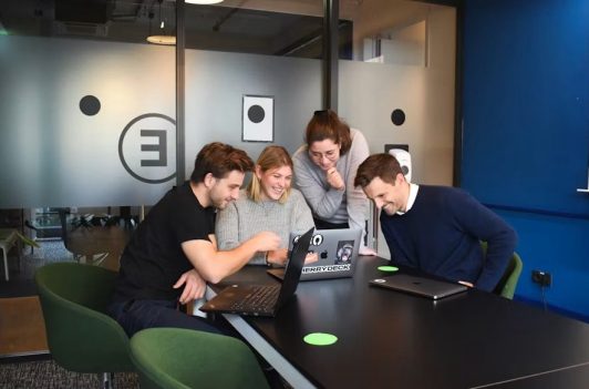 Smiling coworkers collaborating around a laptop to provide expert U.S. Team Support in a modern office setting.