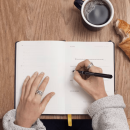 Taking notes for an annual shareholder meeting in a notebook with coffee and a croissant on a wooden table.