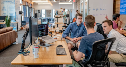 Colleagues discussing Beneficial Shareholder Services at a modern open-office workstation with laptops and monitors.