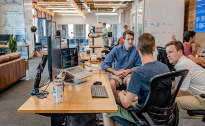Colleagues discussing Beneficial Shareholder Services at a modern open-office workstation with laptops and monitors.