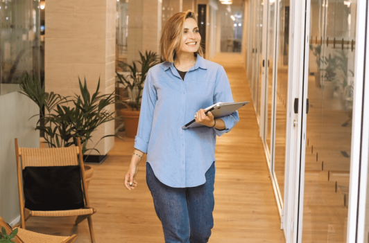 Smiling professional carrying a laptop with client-friendly proofing tools through a modern office hallway.