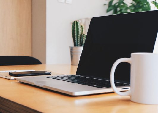 Laptop on wooden desk with coffee mug featuring Easy Edit Technology for a streamlined modern workspace