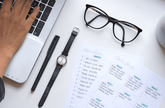 Hand on laptop next to glasses and a planner checklist for SEC filing requirements on a white desk.
