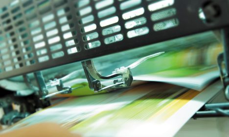 Close-up of a high-speed financial printing press mechanism processing colorful pages of a financial report.